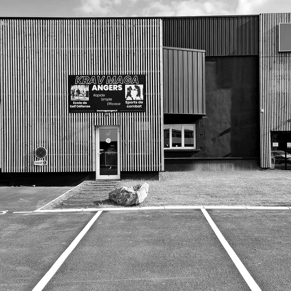 La façade du club : bardage bois, panneau « Krav Maga Angers » au-dessus de la porte, parking marqué au sol juste devant
