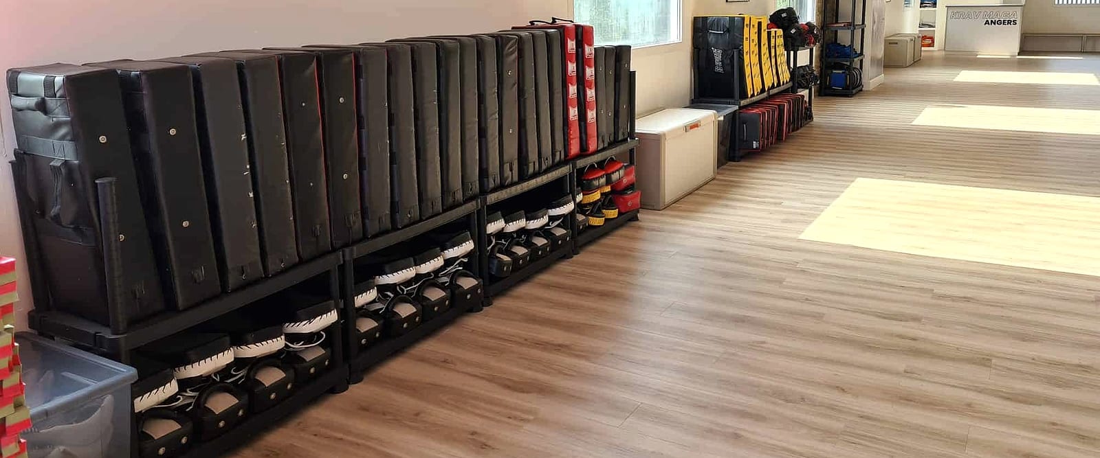 Le matériel du club aligné le long du mur : boucliers de frappe sur leur rack, kettlebells rangées dessous